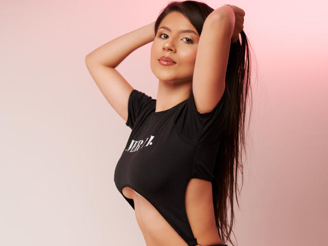 VeronicaRoose with arms up, wearing a black shirt that exposes her sideboob, long dark hair, light skin, subtle smile, pink lighting, soft shadows.