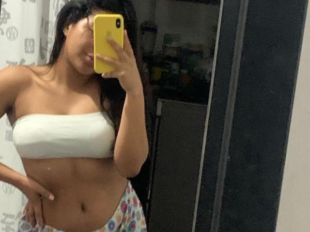 DreamingOfU with medium brown skin, long black hair, white tube top, showing her small tits, holding a yellow phone, wearing colorful pajama pants, taking a mirror selfie.