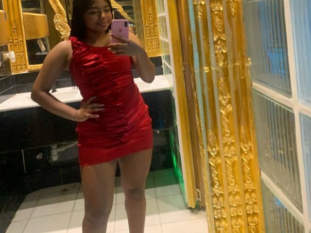 DreamingOfU in a tight red dress, standing with one hand on her hip, holding a pink phone, smiling at her reflection, showing her ass and pussy in the mirror.