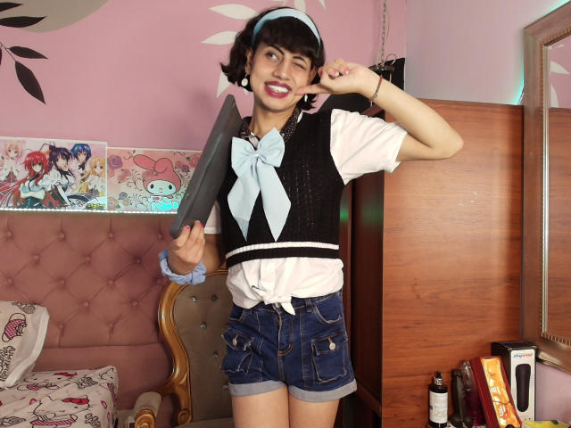 EimyFlorian, cute Asian girl with short black hair, winking, holding a large dildo, wearing a blue visor, black vest, white shirt, blue bow, and denim shorts, smiling.