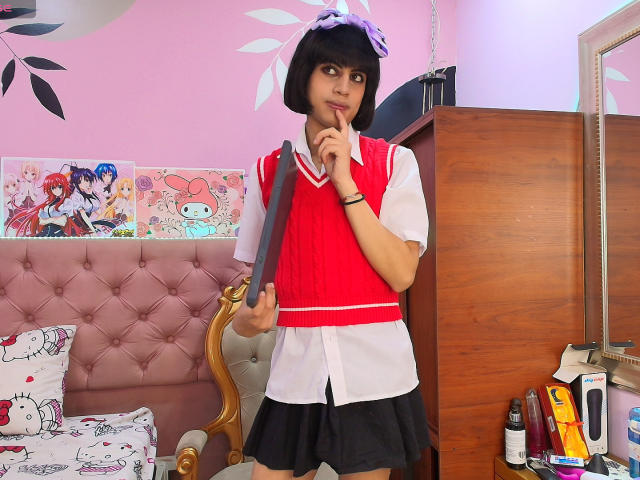 EimyFlorian with short black hair, wearing a red and white schoolgirl outfit, holding a knife to her chin, standing in a pink room, with anime posters in the background.