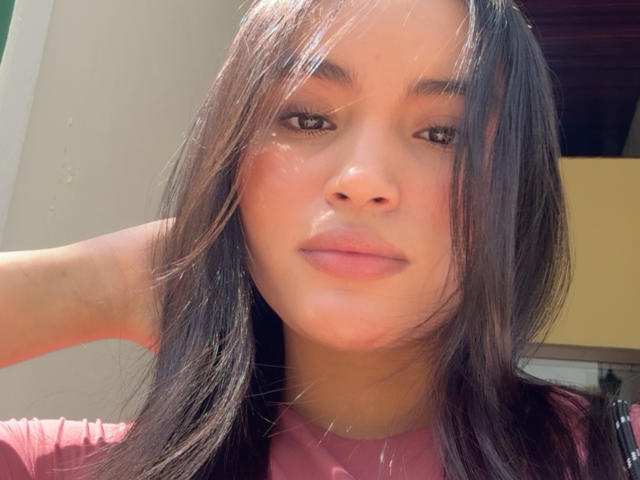 MiiaPalmer a de longs cheveux bruns, une peau claire et des lèvres roses. Elle porte une chemise rose, regarde l'appareil photo avec un léger sourire, et a une expression détendue et confiante..