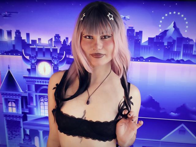 BoniePeach mit rosa und schwarzen Haaren, Sternen-Haarspangen, Nasenring, schwarzer Spitzen-BH, Halskette, hält ein Zopf, lila-blauer Hintergrund, Stadtansicht und Riesenrad im Hintergrund. Brüste, süß, hübsch..