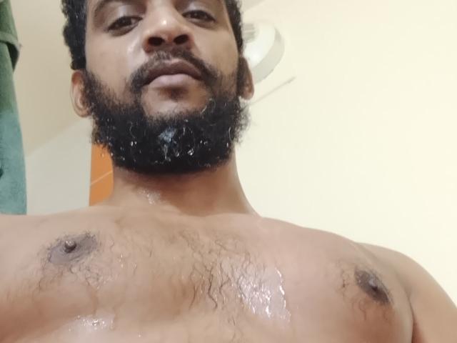Shirtless Didikou69 with wet chest, dark curly beard, and chest hair, gazing down at the camera, showing nipples and a slightly open mouth.