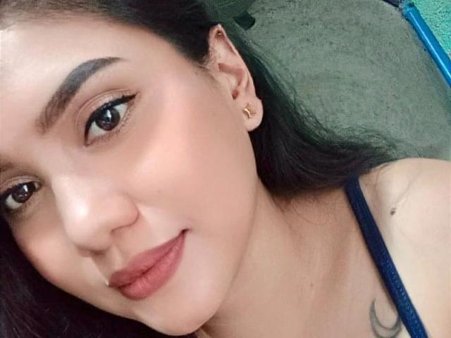 AsianHottie69-hot with brown eyes, dark eyebrows, red lipstick, and a small tattoo on her shoulder. She's wearing a black strap and has gold earrings.