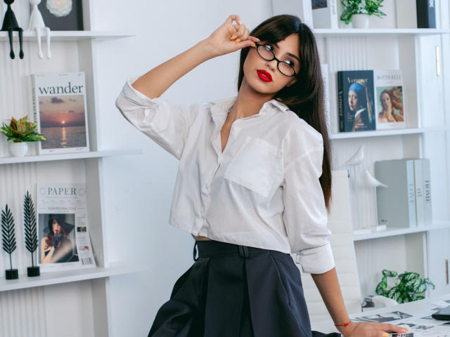 JasmineDay with glasses, white button-up shirt, black skirt, and red lipstick, adjusting her glasses, showing her tits in a bookshelf-filled room. Her ass is barely visible.