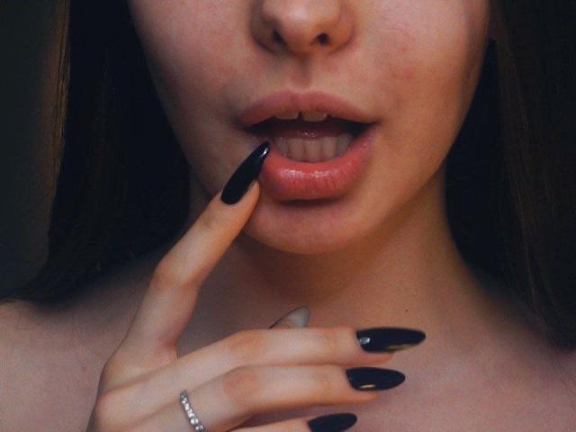 TracyVerbeke's face with glossy black nails, slightly parted pink lips, and a finger touching her lower lip. She's wearing a silver ring on her right hand.