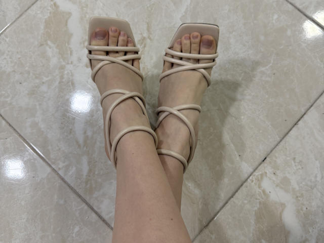 TracyVerbeke's feet in beige strappy high-heeled sandals, showing her toenails with pink nail polish, standing on a shiny tiled floor.