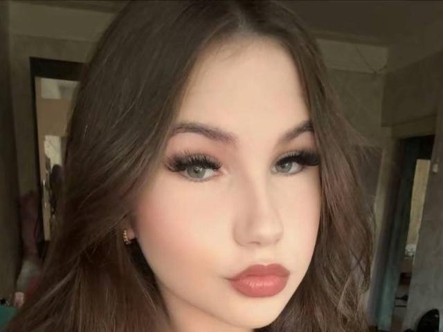 AlbertineWendelken has fair skin, green eyes, and full pink lips. She has long brown hair, thick eyelashes, and is wearing subtle makeup. Her small nose is centered.