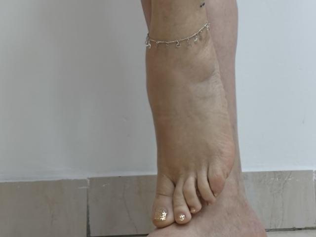 Khharha's tanned leg with a black dragon tattoo, wearing red panties, ankle bracelet, and painted toenails, standing on tiled floor.