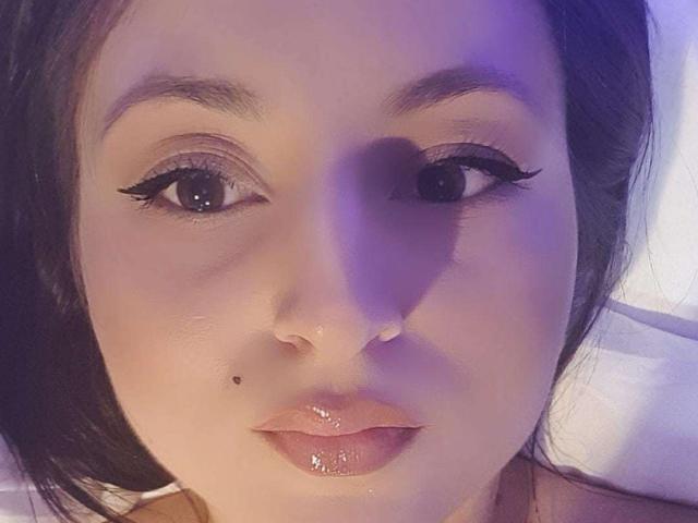 IcameBackIwi has a cute face with dark brown eyes, black eyeliner, shiny pink lips, and a small mole on the right side of her nose. Her skin is fair.