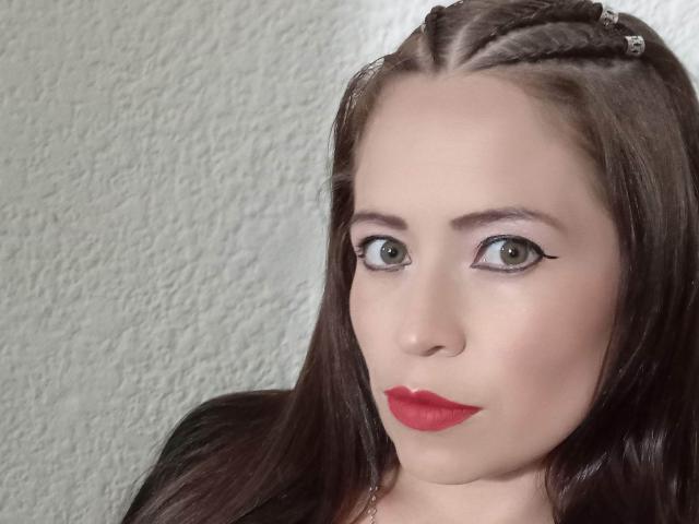 ImEmilyHanks has red lipstick, green eyes, and dark brown hair with a braid. Her makeup includes black eyeliner. Her face is slightly chubby with a fair skin tone.
