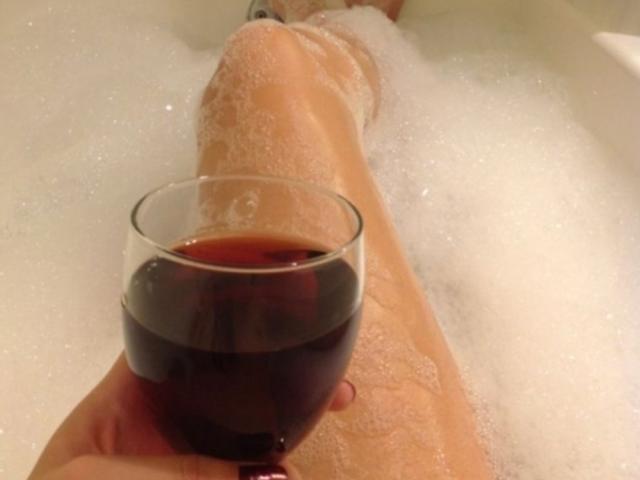 La jambe de HanaMariana est dans une baignoire remplie de bulles, et elle tient un verre de vin rouge de la main droite. Son pied est visible en haut..
