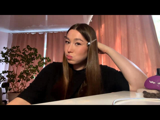 DannaTavorn with long brown hair, pouty lips, black shirt, hand in hair, purple vibrator on table, white ceiling, pink curtains, green plant, white desk, indoor lighting.