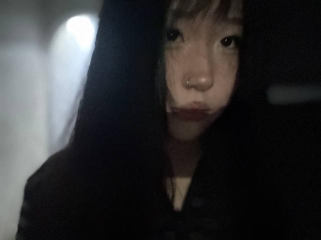JungMcgranor with dark hair, nose ring, and pouty lips, looking straight at the camera in a dimly lit, blurry photo. Her face is the focal point.