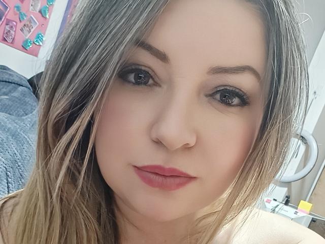 NatalyHami has light skin, brown eyes, and blonde hair, with a nose ring and pink lipstick, looking directly at the camera with a slight, confident smile.