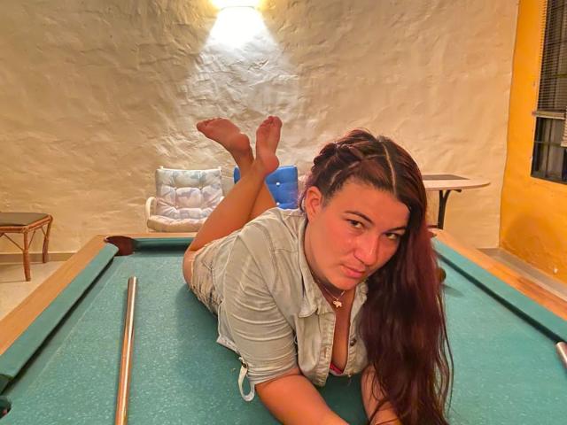 YessiSoto, laying on a green pool table, with her ass up, wearing a gray shirt, brown hair, and a necklace, looking at the camera with a pouty face.
