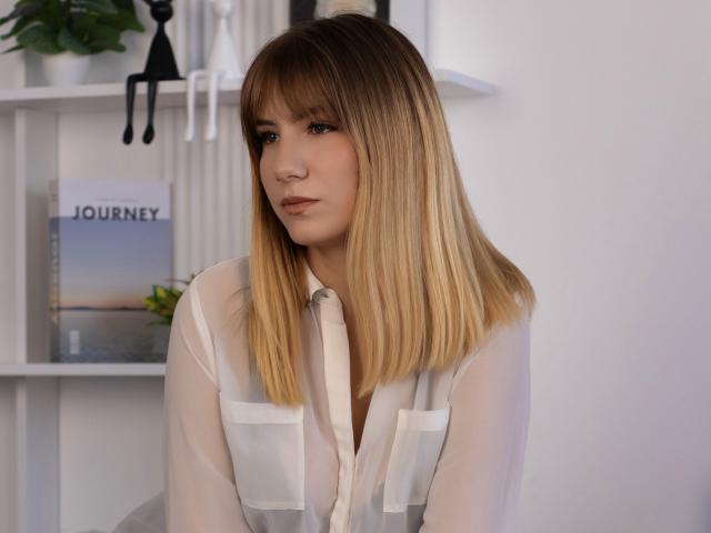 Chloe Kingsley mit blondem Bob, weißem, transparenten Hemd, sanftem Ausdruck, mittlerer Brustgröße, leicht geöffneten Lippen, in einem hellen Raum, die zur Seite schaut, mit dezentem Make-up..