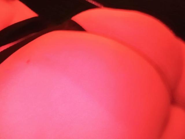 El trasero grande y rojo de OnixDamon es el foco principal, con una correa negra que se ve parcialmente en la parte superior izquierda. La piel es suave y la luz es cálida..