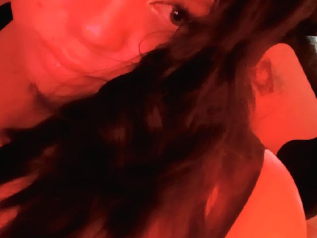 El rostro de OnixDamon, con una ligera sonrisa, parcialmente oculto por el cabello negro largo y ondulado, bajo una iluminación roja. Se puede ver el ojo de OnixDamon, y están sin camisa, con los hombros desnudos..