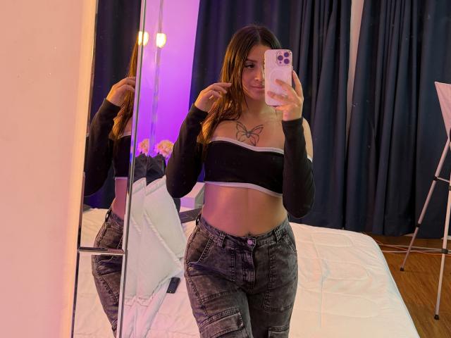 LunnaBlossom with long brown hair, black strapless top, butterfly tattoo, and ripped jeans, taking a mirror selfie, showing her flat stomach and small tits.