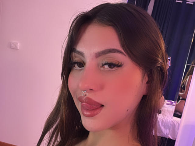 LunnaBlossom has dark brown hair, a nose ring, and is sticking her tongue out with long, winged eyelashes. Her skin is light with a pinkish hue.