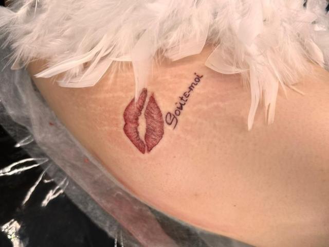 CicelyDence's ass has a realistic red lipstick tattoo with "goilicomme" written in cursive above it, surrounded by white feather-like texture.