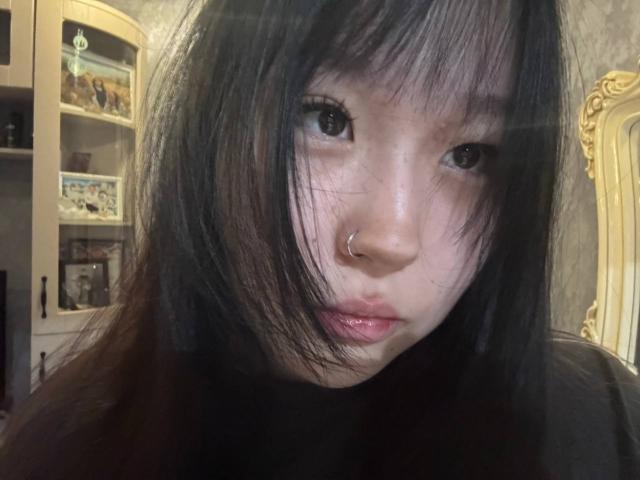 JungMcgranor with black, straight, shoulder-length hair, a nose ring, and slightly parted, shiny pink lips. Her brown eyes are focused on the camera. She looks serious and cute.