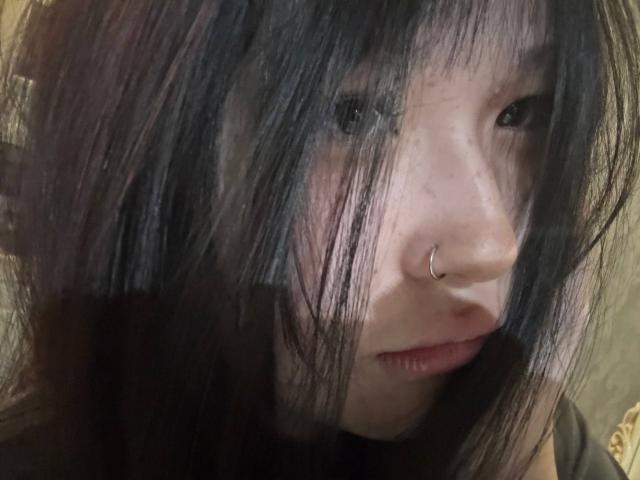 JungMcgranor has dark, messy black hair covering one eye, a small nose ring, and a serious expression. She's looking slightly to the side with visible pink lips.