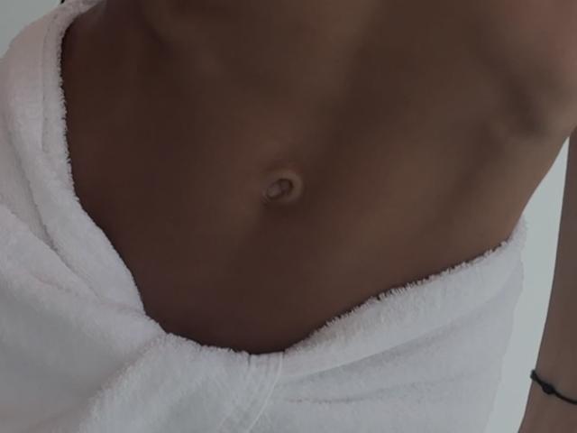 Fridaa's bare, toned, brown-skinned belly with a small navel, wrapped in a white towel, showing her flat, sexy abs. She has a black bracelet on her right wrist.