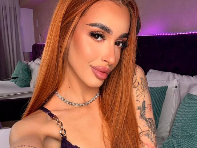 MarissaFex tiene el pelo largo y naranja, cejas gruesas y un piercing en la nariz. Lleva un sujetador morado con tirantes dorados, un collar de diamantes y tiene un tatuaje en el brazo..