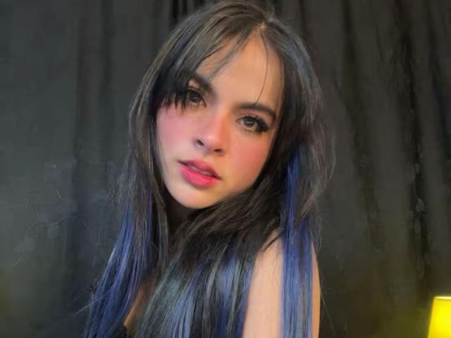 SophieBanksX has long, dark, blue-tinted hair, pink lips, and a slightly curious expression. She's looking at the camera with soft, natural light on her face.