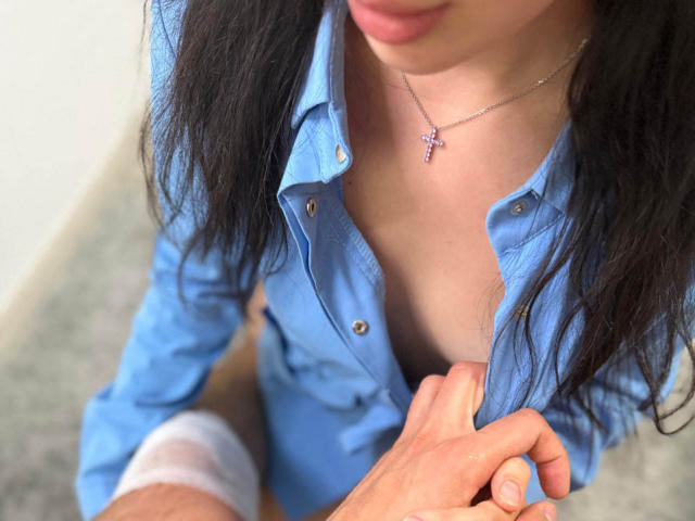LeaMike's blue shirt is open, showing her tits, with a hand gripping her chest. She has black hair, a cross necklace, and a bandaged knee.