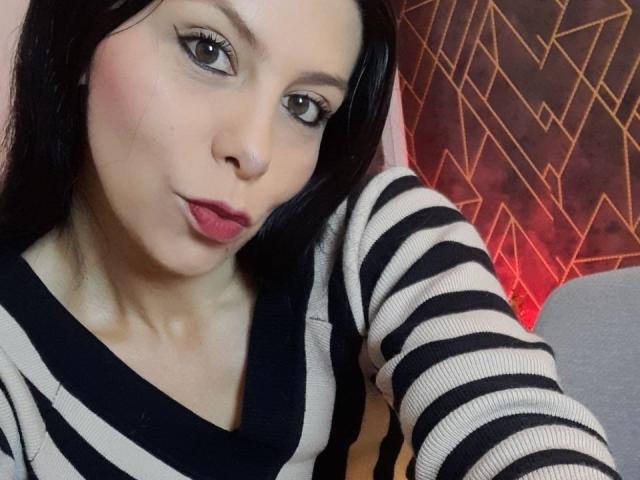 KarlaMazuera with black hair, wearing a striped black and white top, pouting with pink lips, light skin, and eyeliner. She has a cute face and a subtle smile.