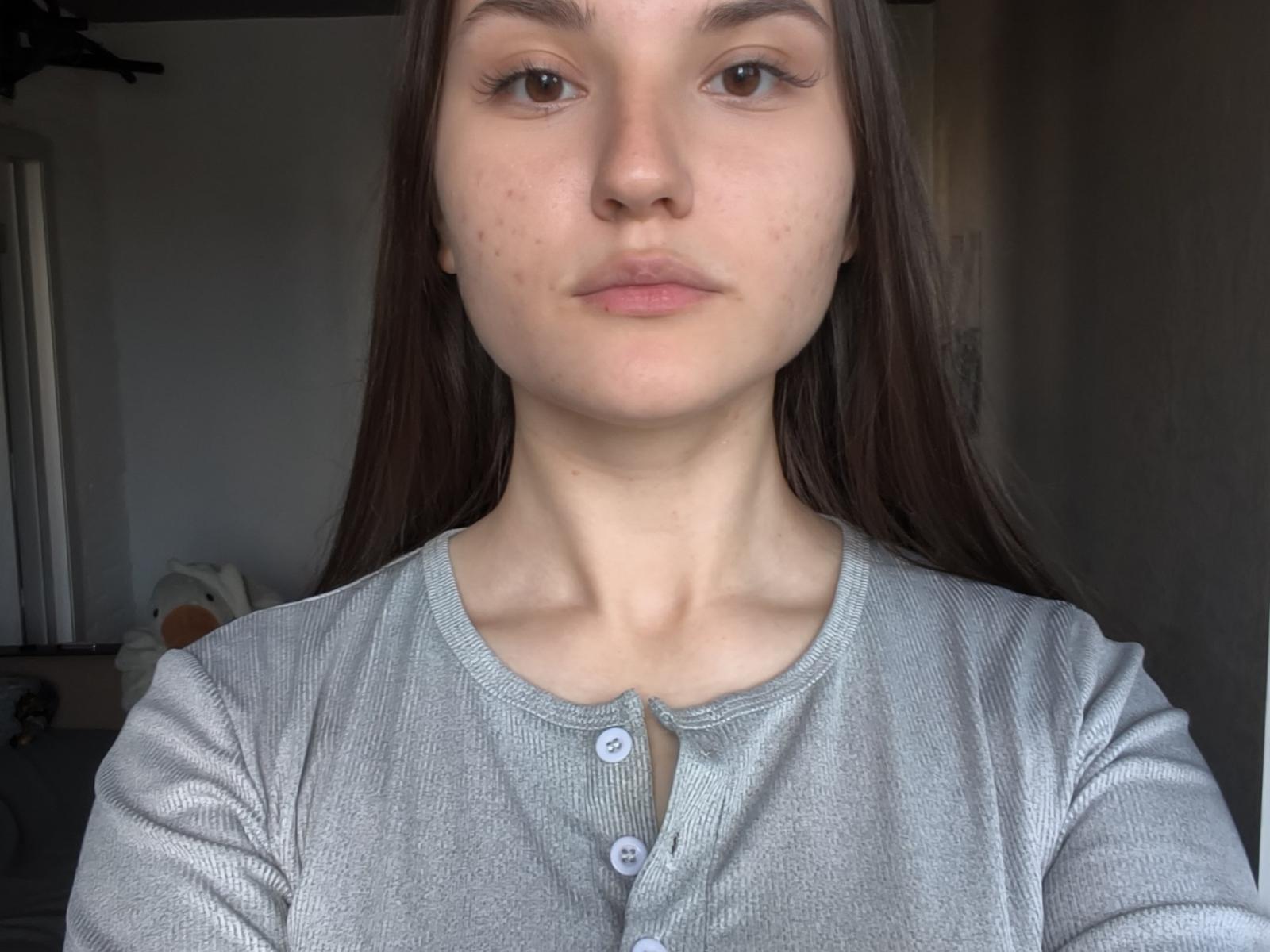 CathrynJacquet has a serious face, long brown hair, light skin, and small acne spots. She's wearing a gray ribbed button-up shirt, with her tits not visible.