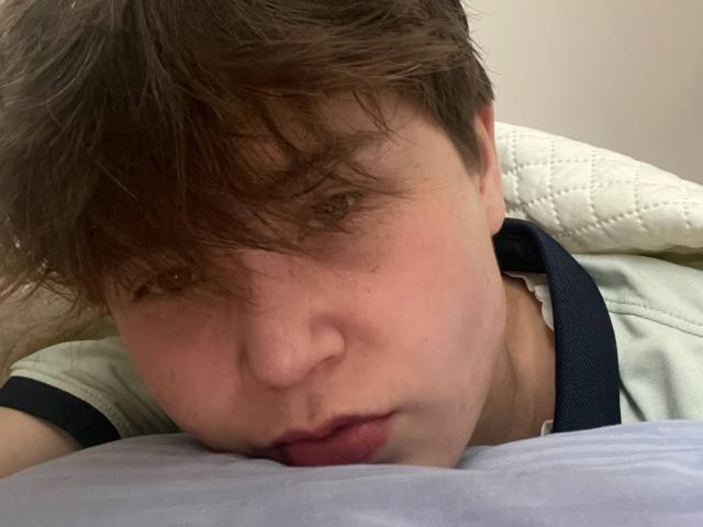 MarybelleDoerr's face is buried in a pillow, her brown hair messy, lips slightly parted, wearing a green and black shirt, with a quilted pillow behind her.