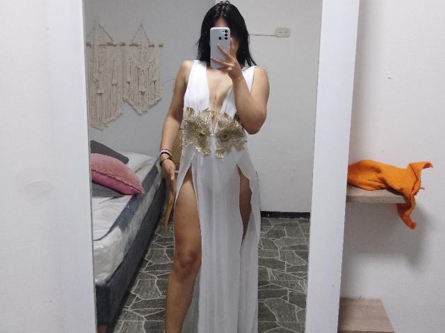 PaulhettJoens in a white dress with a deep cleavage, gold floral belt, and high slits, showing her thick thighs and curvy ass, taking a mirror selfie.