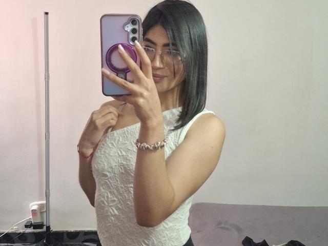 PaulhettJoens with medium tits, wearing a white lace sleeveless top, glasses, and a bracelet, taking a mirror selfie with a purple pop socket on her phone.