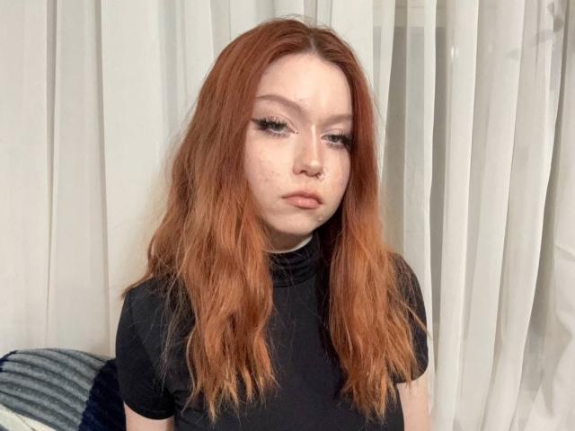 LilliamChevalier has red hair, a nose ring, and is wearing a black top. She has freckles, long eyelashes, and a serious expression. Her tits are not visible.