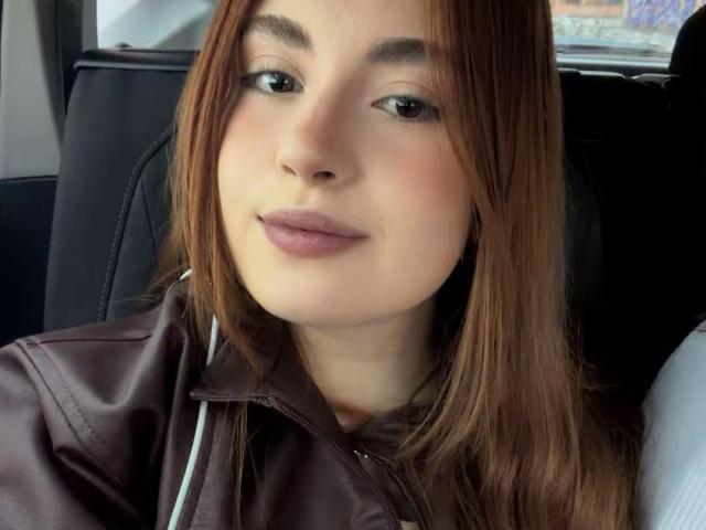 VicluX ha i capelli castani, la pelle chiara e labbra piene con un leggero rossetto rosa. Indossa una giacca di pelle marrone ed è seduta in un'auto con sedili neri..