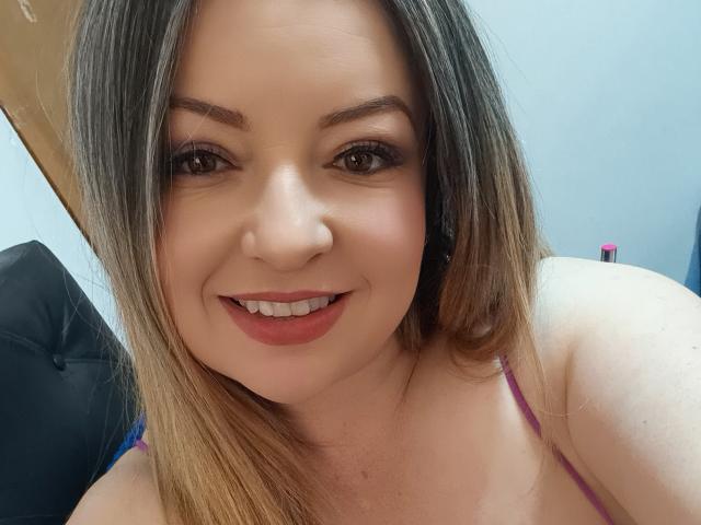 NatalyHami has medium-length brown hair, brown eyes, and a smile showing pink lipstick. She's wearing a pink strap and has a cute, sexy face.