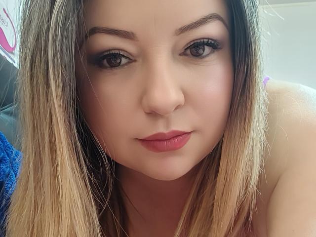 NatalyHami's face, showing her blonde hair, brown eyes, and pink lips with a slight smile, looking directly at the camera. She has fair skin and a subtle makeup look.