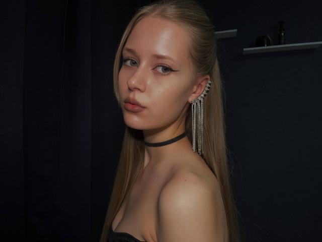 LillianaWhang has long blonde hair, light skin, and wears a black choker with dangling earrings. She's looking to the side with subtle makeup and a slight pout.