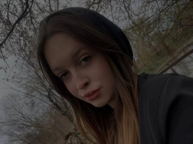 O rosto de Priscila Nagelhout, com cabelos castanhos longos, lábios levemente entreabertos e um gorro preto, vestindo uma blusa escura, olhando para baixo com uma expressão pensativa. Suas nádegas não estão visíveis..