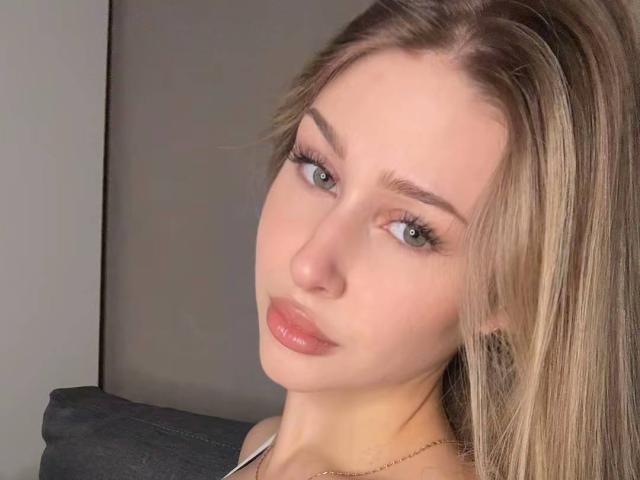 Milagros Edmisten a les cheveux blonds, les yeux bleus et des lèvres roses brillantes. Elle regarde l'appareil photo avec un léger sourire, et porte un fin collier en or. Ses seins ne sont pas visibles..