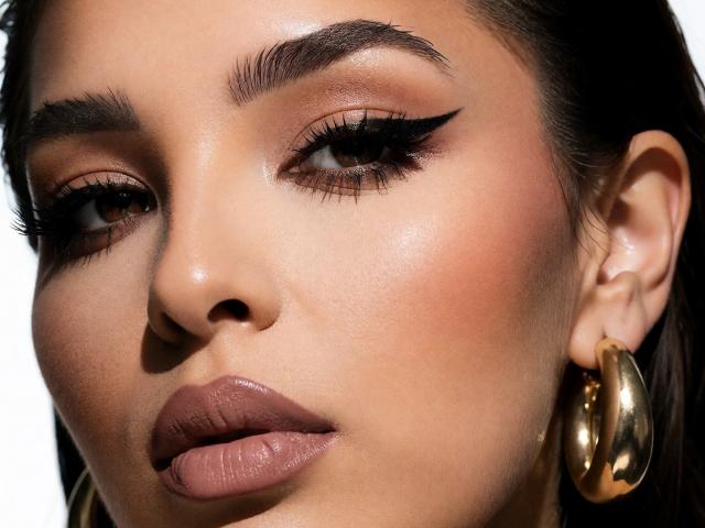 KayaOcean's face with glossy brown lips, thick black eyeliner, and golden hoop earrings. She has dark brown skin, full eyebrows, and long eyelashes. Her expression is slightly pouty.