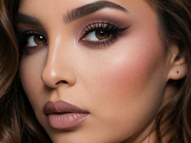 KayaOcean's face, featuring brown eyes, thick eyebrows, dark mascara, pinkish-brown eyeshadow, glossy brown lips, and wavy brown hair, with a smooth, slightly tanned complexion.