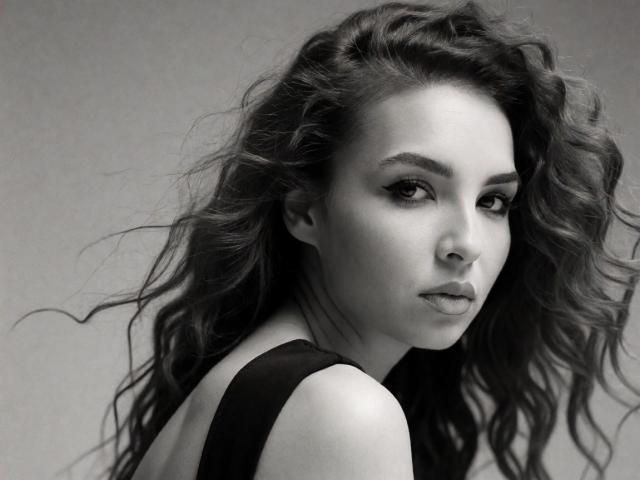 KayaOcean has wavy, dark hair, a serious face, and is looking over her shoulder. She's wearing a black top, and her tits are partially visible. Black-and-white photo.