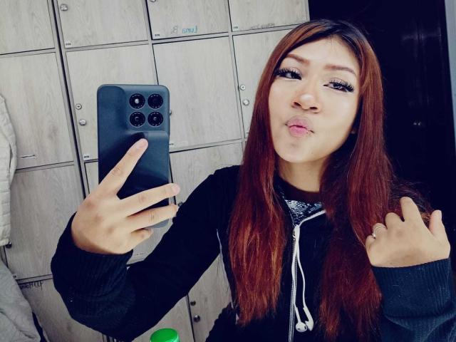 BonnieBodn with long red hair, black hoodie, and full lips pouting, takes a selfie with a black iPhone, holding her phone with one hand and her hair with the other.