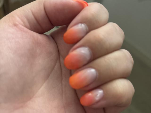 ElvinnaLaFrancaise's hand with orange-tipped, glossy, almond-shaped nails, showing off her shiny, well-manicured fingers and smooth, fair skin.